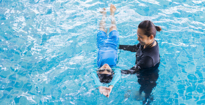 Girl learning to swim with coach at the leisure center