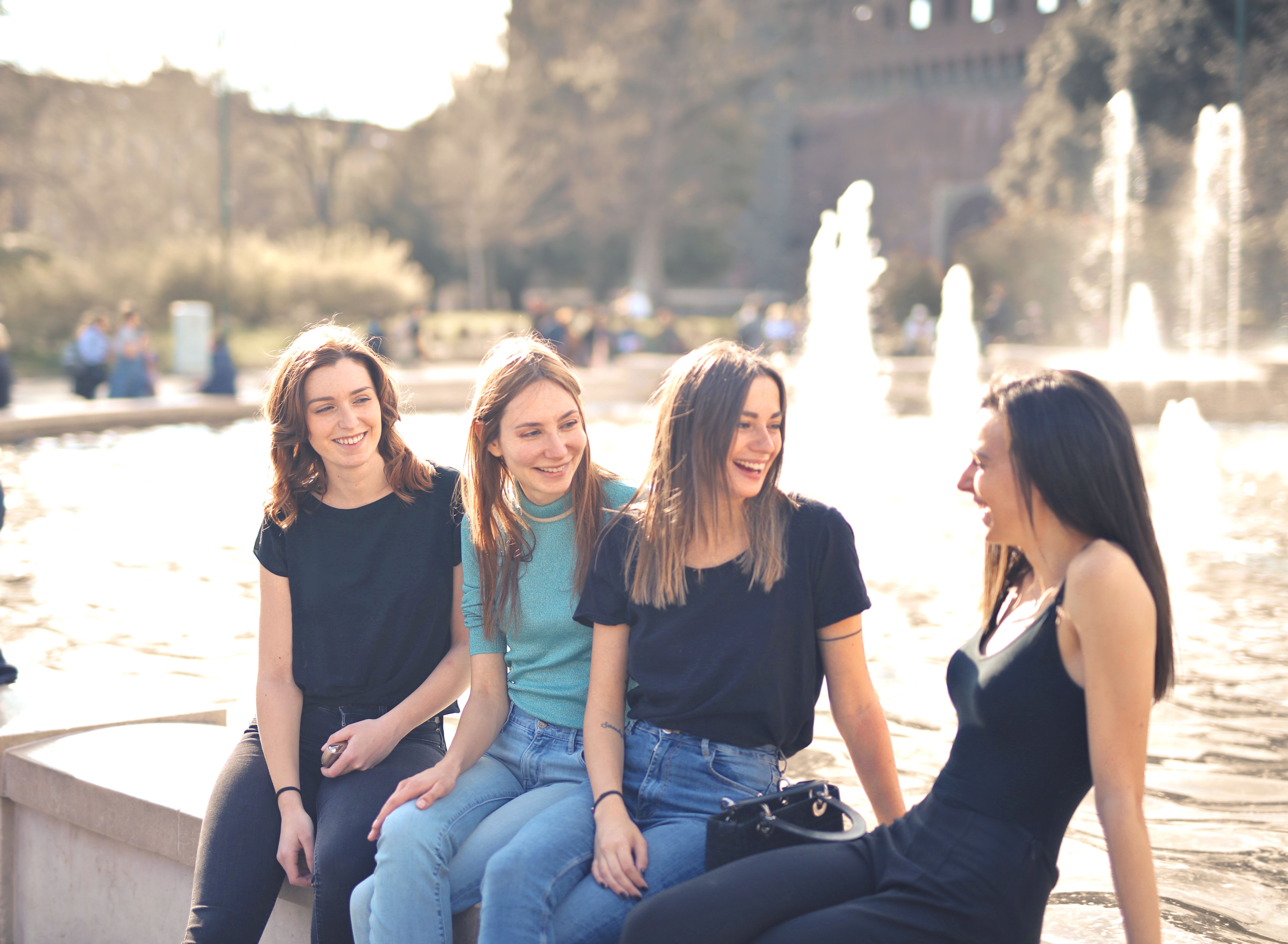 Four friends laughing and chatting together outdoors on a sunny day