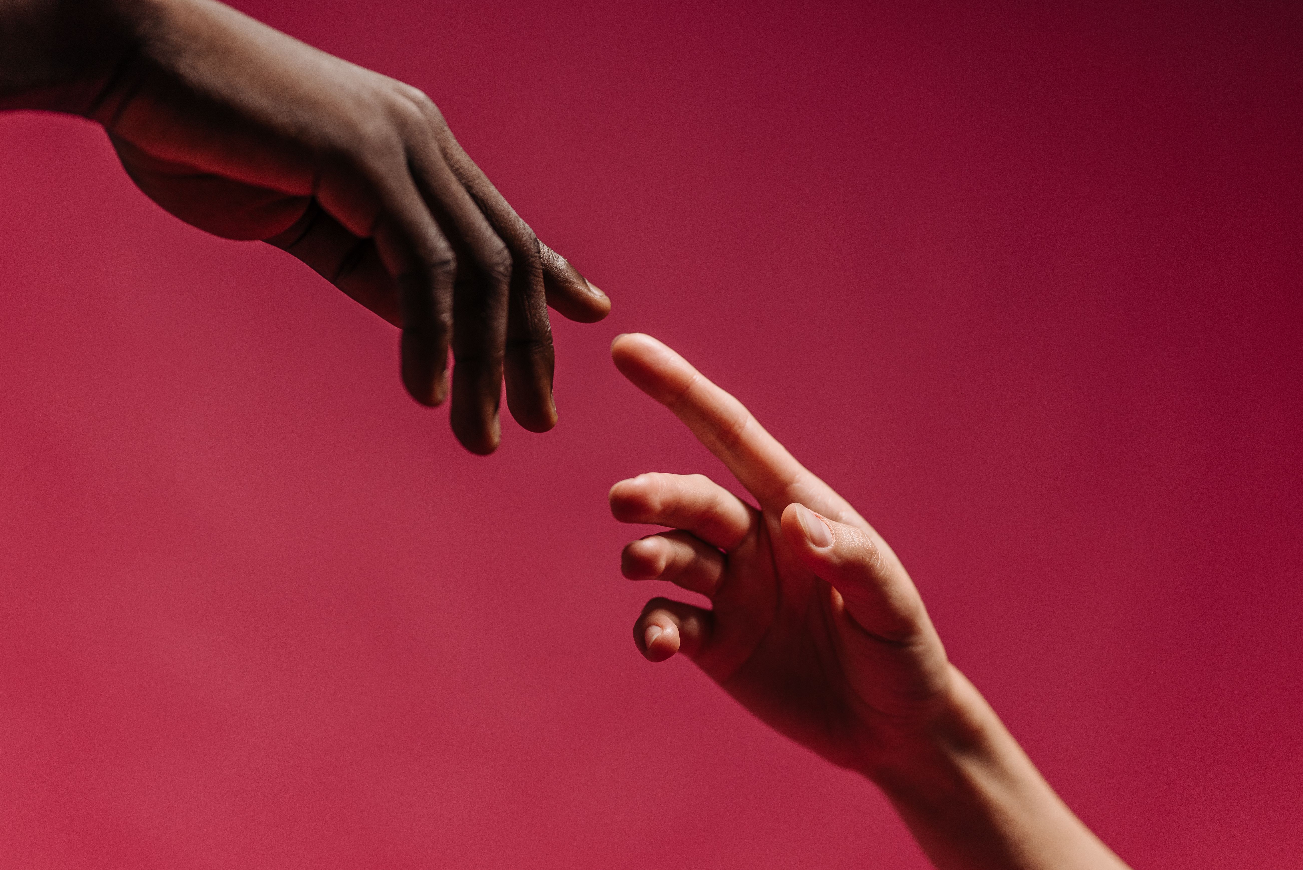 Two hands reaching toward each other against a vibrant red background, symbolizing deep human connection
