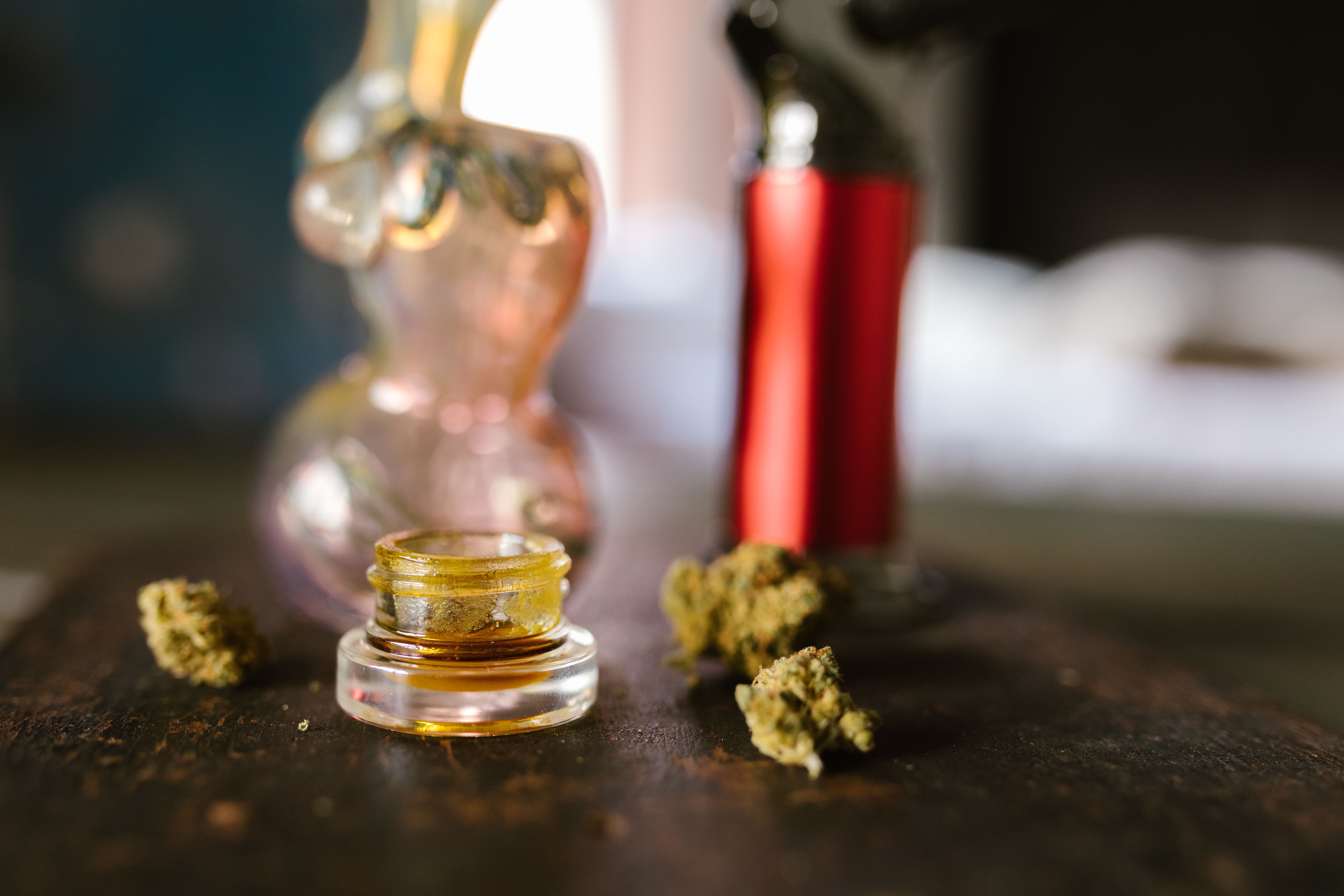 Glass jar of cannabis concentrate like live resin surrounded by flower and accessories