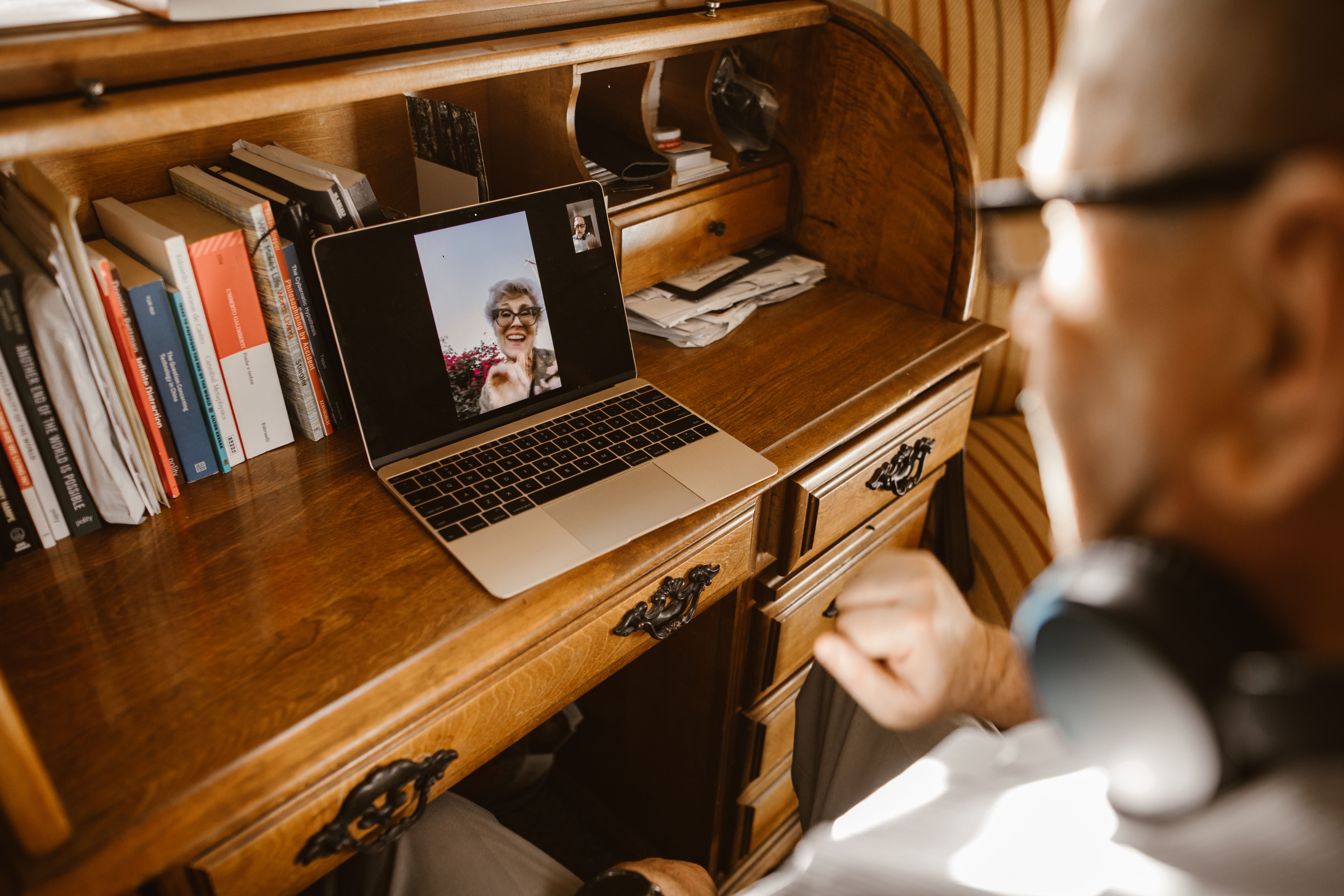 An elderly man video calling a loved one on a laptop, using technology to bridge distance